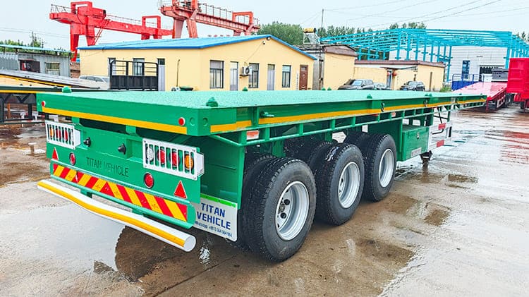 Flat Deck Trailer Price: 9500USD The flat deck trailer for sale is designed to accommodate both 20-foot and 40-foot containers, making ideal for efficient transport between ports and inland locations. The tri axle flat deck trailer for sale are engineered with structural balance in mind. When loaded, the weight is evenly distributed across the frame, minimizing concentrated stress points and reducing the chances of long term structural deformation or fatigue.  Specification of Flat Deck Trailer Dimension: 12500mm*2500mm*1630mm Loading capacity: 60 ton Side Beam: 160mm high Axles: 3 axles, TITAN brand, 13 ton Tire: 11R22.5, 12 units Suspension: mechanical suspension Leaf Spring:10 layers Bumper: 4mm thickened bumper Landing Gear: 28 ton, JOST brand Lamp: LED lamp with anti-theft net  Shipping of Flat Deck Trailer for Sale Before these 40 foot flat deck trailers are delivered, each unit undergoes thorough waterproof treatment to ensure durability during sea shipping. A protective wax layer is first applied to the surface of the flat deck trailer body which is followed by a complete waterproof cover, which offers dual-layer defense against seawater corrosion and humid salt air, conditions frequently encountered during maritime transport. Depending on buyer preferences, the tri axle flat deck trailer for sale can be transported via container shipment or roll-on/roll-off (RoRo) vessels.  Advantage of Flat Deck Trailer At the heart of the flat deck trailer for sale strength is the main beam, which is made of Q355 low-carbon, high-strength alloy steel. The material boosts the 40 foot flat deck trailer capacity to endure heavy duty loading. The key joints and frame components are welded using automatic submerged arc welding, a process that ensures deep penetration and uniform welds that not only improves structural integrity but also extends the flat deck trailer life span under demanding usage. Additional reinforcement is applied to high-stress zones, such as the gooseneck area. A double-layered steel plate is used in these sections to further increase the load-bearing ability. The structural enhancement is especially valuable when transporting bulky or concentrated cargo, as prevents bending or warping under pressure. Surface finishing is another aspect where attention to detail is evident. The tri axle flat deck trailer for sale is treated with a powder coating followed by a high-temperature baking paint process. Though the method involves higher costs compared to standard painting, it offers better resistance to scratching, sun fading, and peeling. The treatment reduces the need for frequent repainting, thereby lowering long term maintenance costs. The flat deck trailer for sale features an open deck platform, which greatly simplifies the loading and unloading of different cargo types. The flexibility is particularly useful in coastal regions like Senegal, where diverse freight conditions exist.  Since the deck is exposed to frequent contact and wear, TITAN uses a patterned steel plate on the surface to provide both durability and better traction. The deck material, 3mm thick high-strength alloy steel, is selected for its excellent load support and resistance to rust, helping the trailer retain its appearance and functionality in moist or saline environments. Each axle on the 40 foot flat deck trailer is rated to handle 13 tons, providing strong support for high-capacity freight. These axles are built to resist bending and fatigue, and they perform reliably on gravel or uneven roads. The durable construction helps mitigate damage from vibration and prevents failures caused by consistent overloading or repeated impacts. The suspension system also plays a critical role in performance. The 40 foot flat deck trailer uses a mechanical suspension setup with multi-leaf springs and a 70mm central balance pin. Reinforcements on all sides—front, rear, and both flanks—help maintain form and absorb shocks effectively. The robust suspension configuration ensures stability and preserves the structural frame even under the heat and rough terrain commonly found in Senegal. In addition, the lighting system on the tri axle flat deck trailer for sale has been thoughtfully upgraded. It includes a complete set of LED lights, which outperform traditional bulbs in energy use, brightness, and lifespan. These LEDs are resistant to shaking and moisture, ensuring better visibility in Senegal poor weather or during nighttime operations. TITAN also integrates an anti-theft feature into the lighting system, offering an added level of security when the flat deck trailer for sale is parked or in transit.